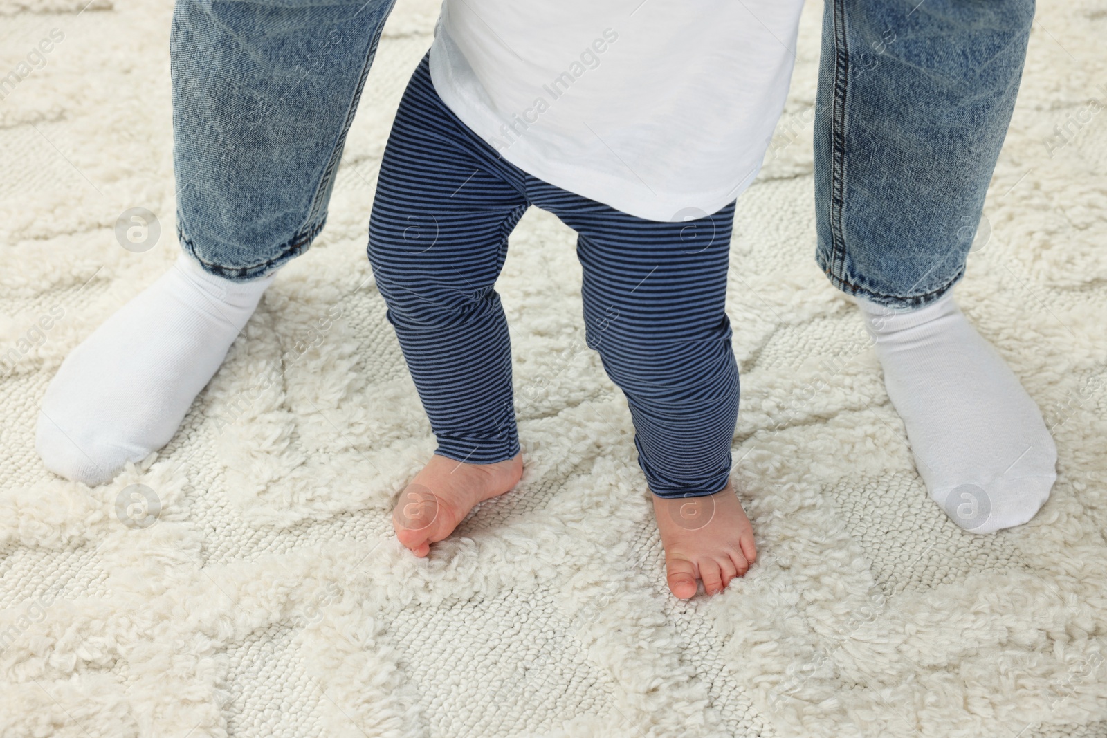 Photo of Mother supporting her son while he learning to walk on carpet, closeup