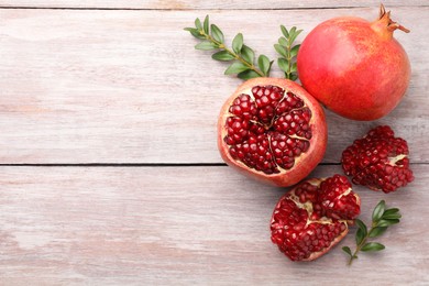 Fresh pomegranates and green leaves on wooden table, flat lay. Space for text