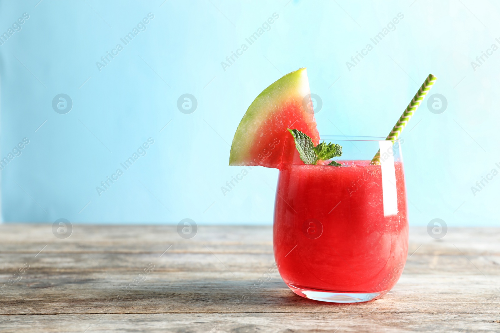 Photo of Tasty summer watermelon drink in glass on table against color background. Space for text