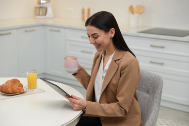 Photo of Young woman with tablet having breakfast in kitchen. Morning routine