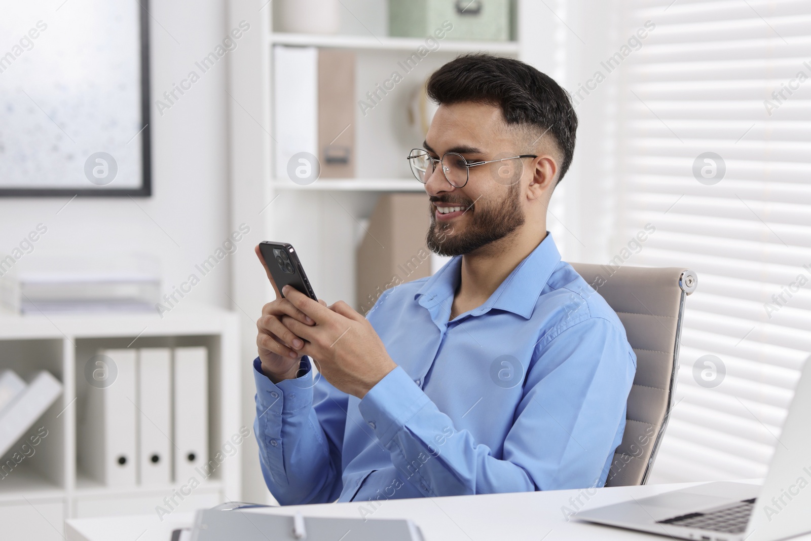 Photo of Happy young man using smartphone at white table in office