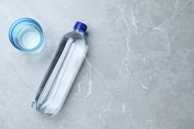 Glass and plastic bottle with water on grey background, flat lay. Space for text