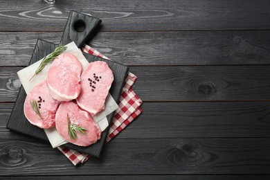 Photo of Pieces of raw pork meat and spices on black wooden table, top view. Space for text