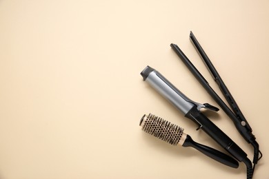 Photo of Curling iron, hair straightener and round brush on beige background, flat lay. Space for text
