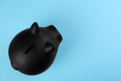 Black piggy bank on light blue background, top view. Space for text