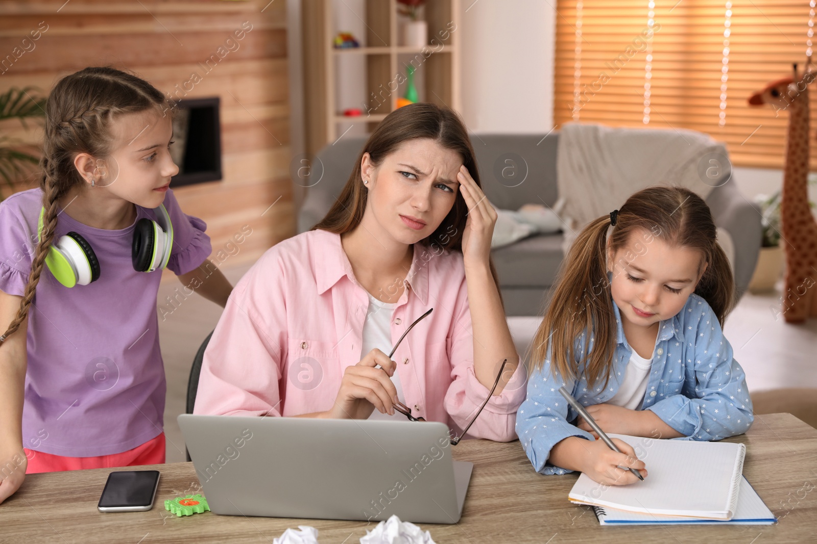 Photo of Children disturbing stressed woman in living room. Working from home during quarantine