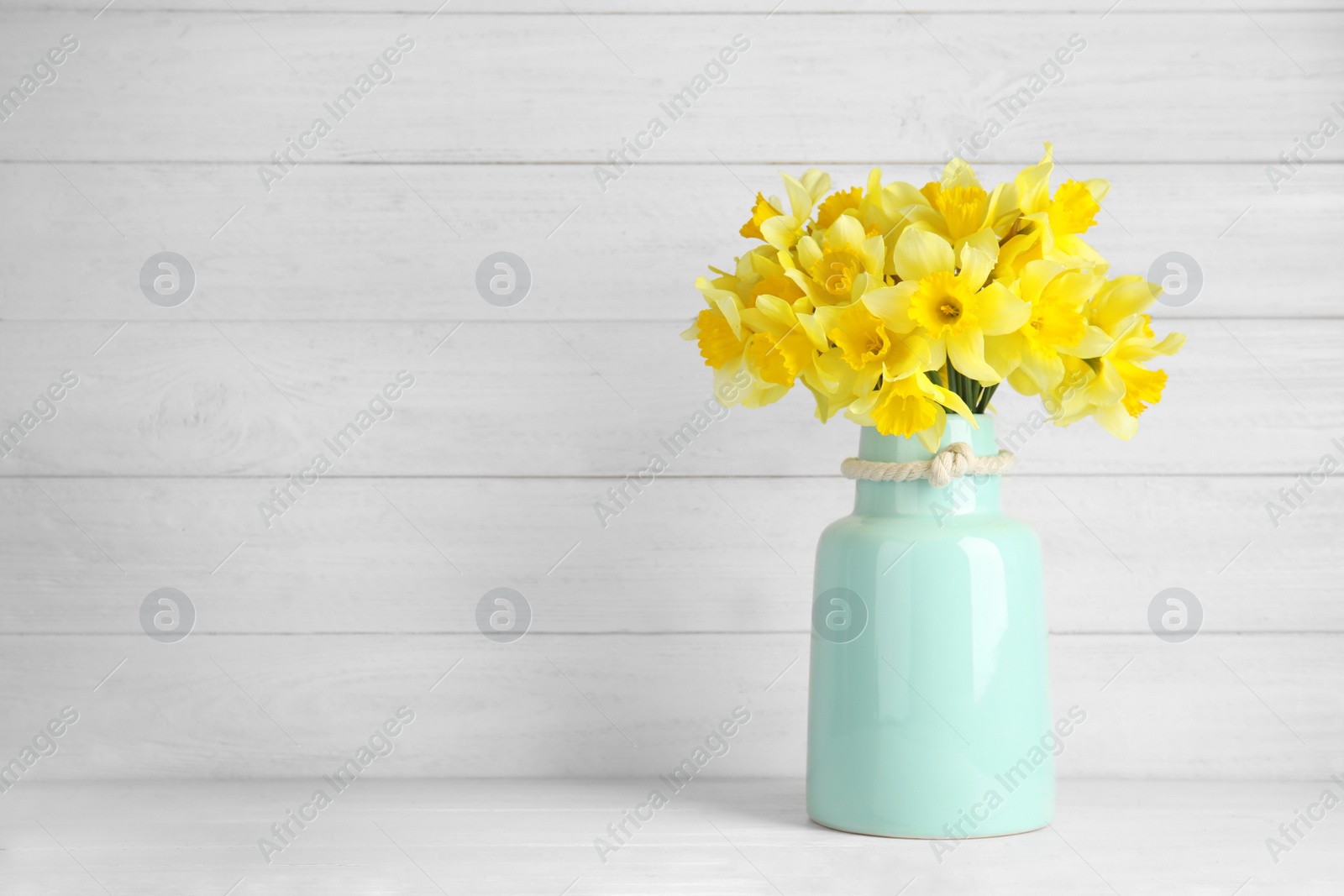 Photo of Bouquet of daffodils in vase on table against wooden background, space for text. Fresh spring flowers