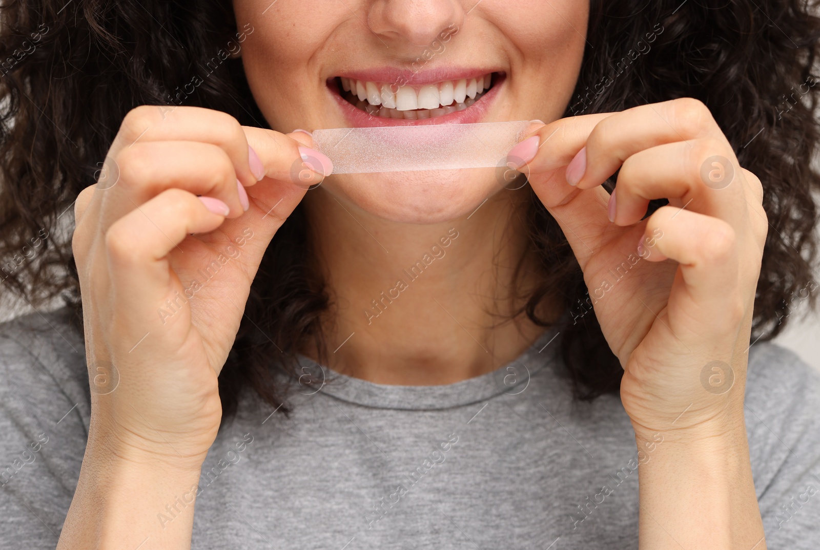 Photo of Young woman holding teeth whitening strip, closeup