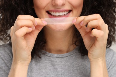 Photo of Young woman holding teeth whitening strip, closeup