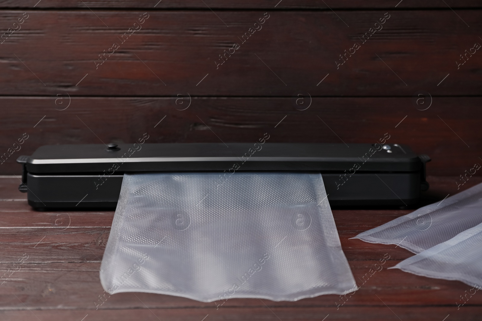 Photo of Sealer for vacuum packing with plastic bags on wooden table