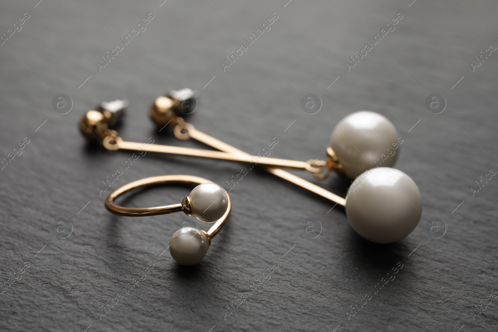 Photo of Elegant golden ring and earrings with pearls on black table, closeup