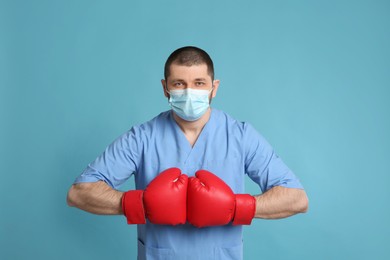 Photo of Doctor with protective mask and boxing gloves on light blue background. Strong immunity concept