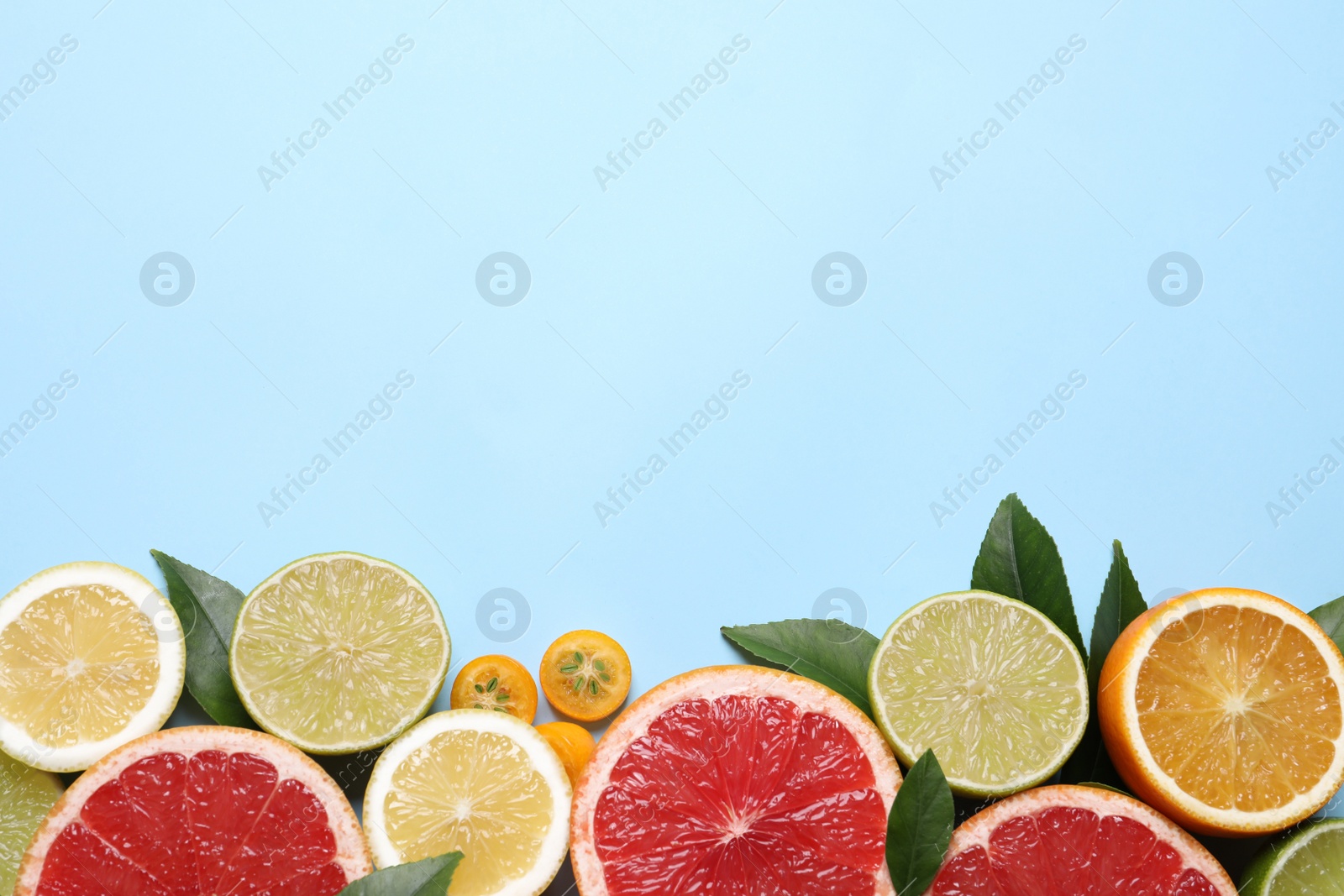 Photo of Fresh juicy citrus fruits with green leaves on light blue background, flat lay. Space for text