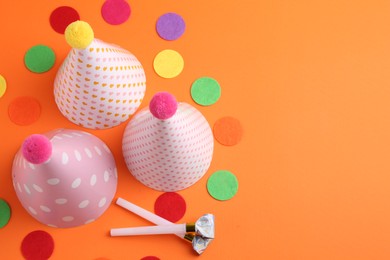 Party hats and other bright decor elements on orange background, flat lay. Space for text