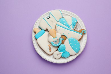 Plate of baby shower cookies on lilac background, top view