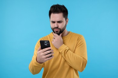 Young man using smartphone on light blue background