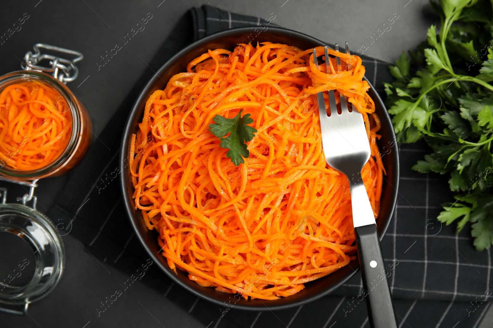 Photo of Delicious Korean carrot salad and parsley on black table, flat lay