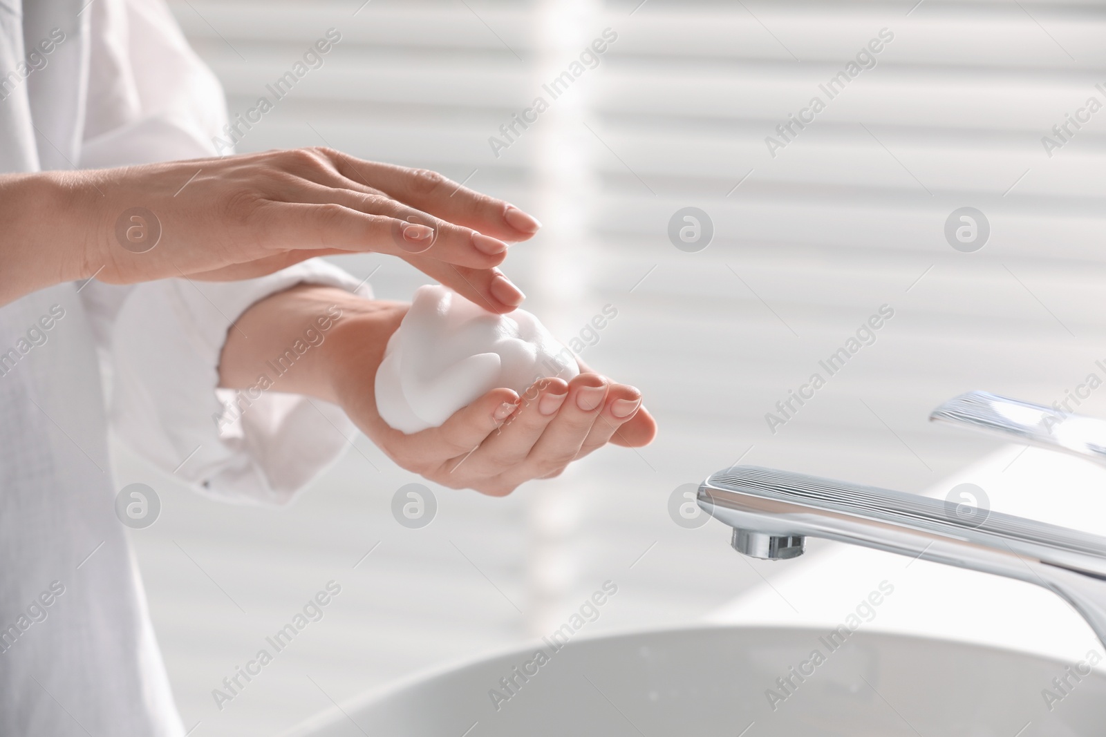 Photo of Woman washing hands with cleansing foam near sink in bathroom, closeup