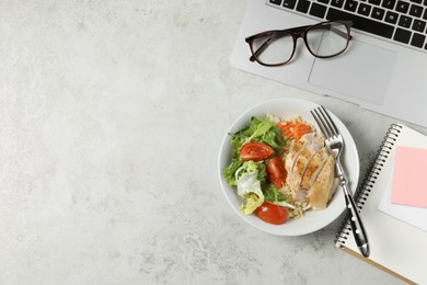 Photo of Bowl of tasty food, laptop, glasses, fork and notebook on light grey table, flat lay with space for text. Business lunch
