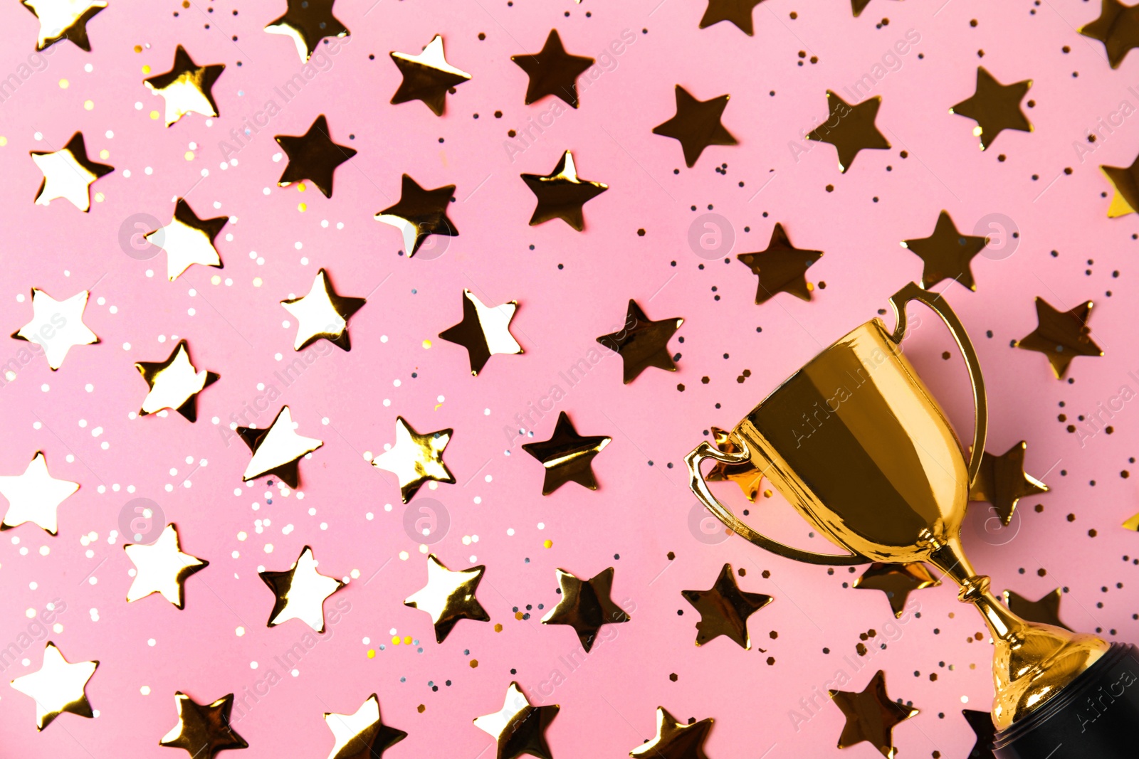 Photo of Gold trophy cup and confetti on light pink background, flat lay. Space for text