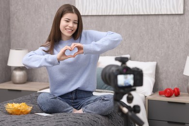 Photo of Smiling teenage blogger making heart gesture to her subscribers while streaming at home