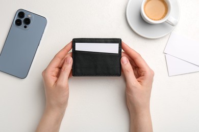 Photo of Woman holding leather business card holder with blank card at white table, top view