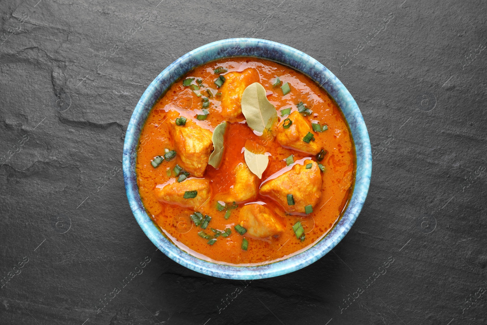 Photo of Bowl of delicious chicken curry on black table, top view