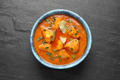 Photo of Bowl of delicious chicken curry on black table, top view