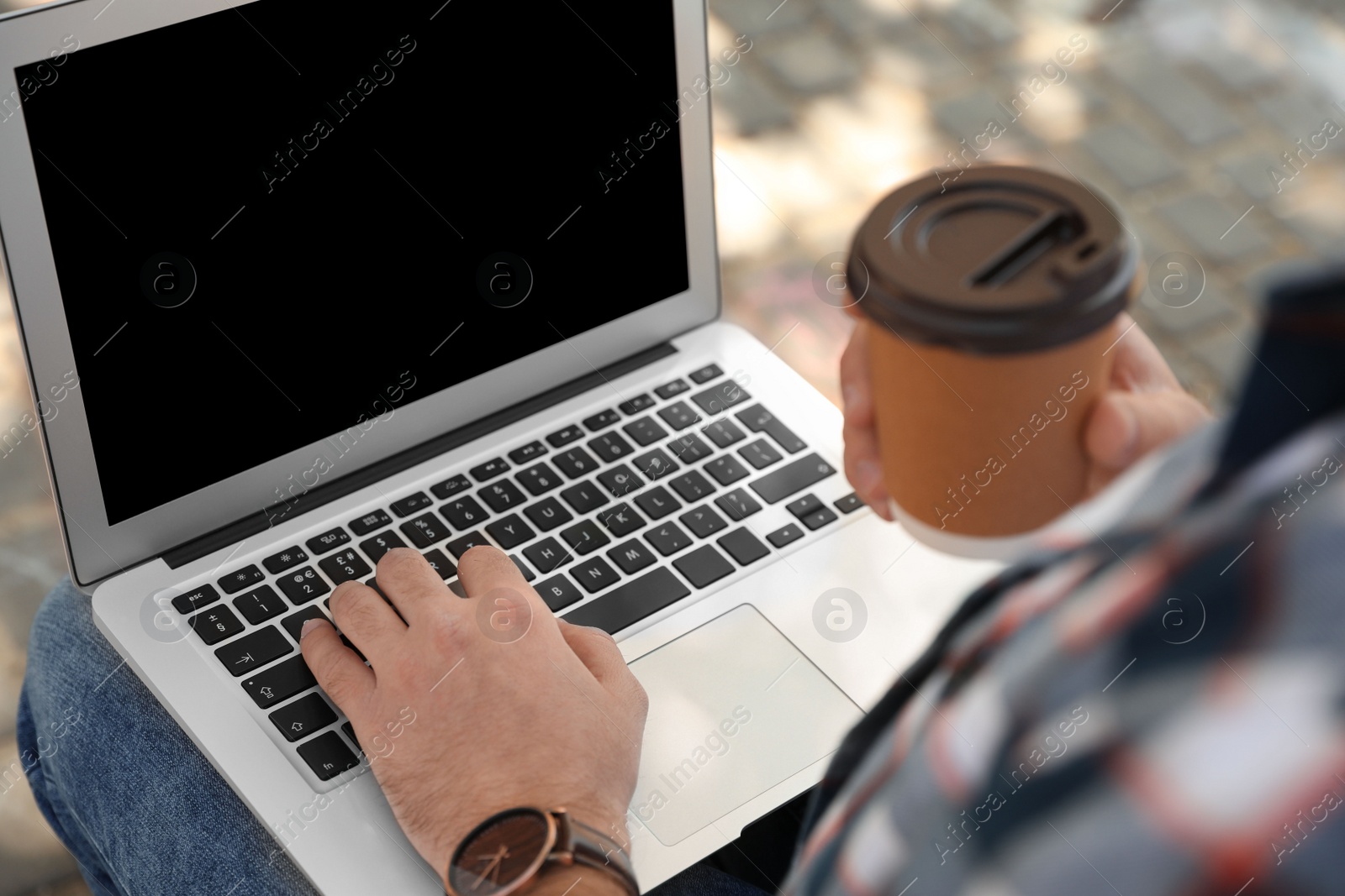 Image of Young man with paper cup of coffee working on laptop outdoors, closeup