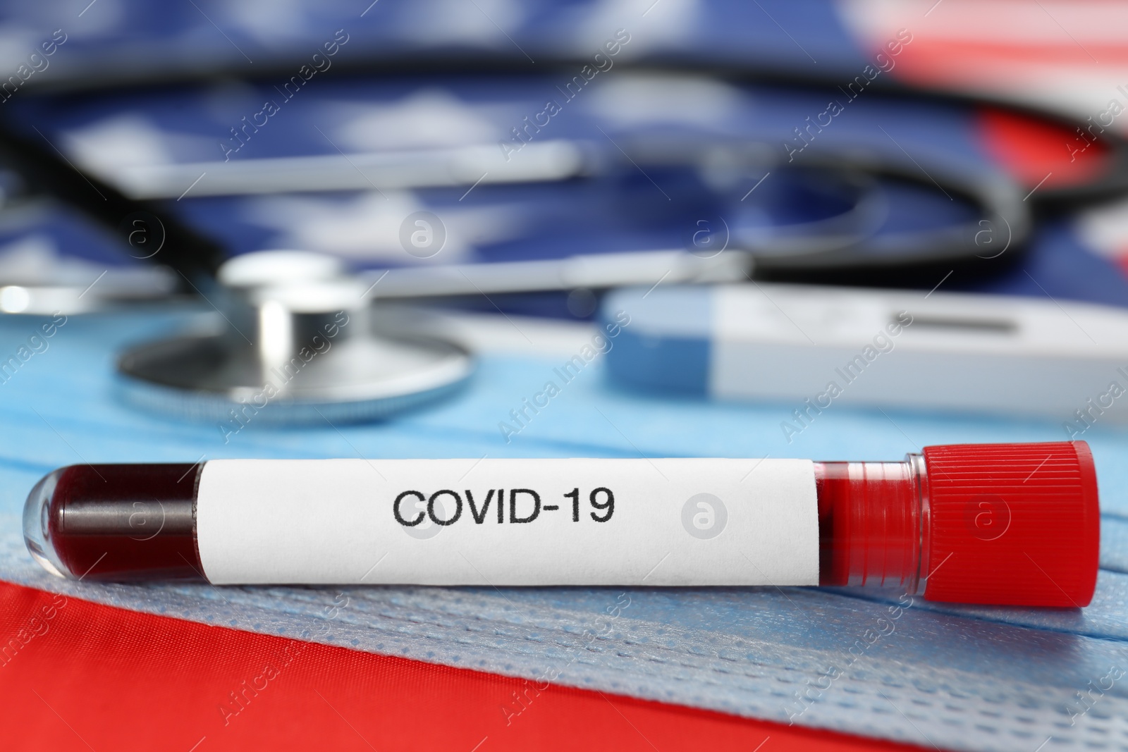 Photo of Test tube with blood and protective mask on American flag, closeup. Coronavirus pandemic in USA