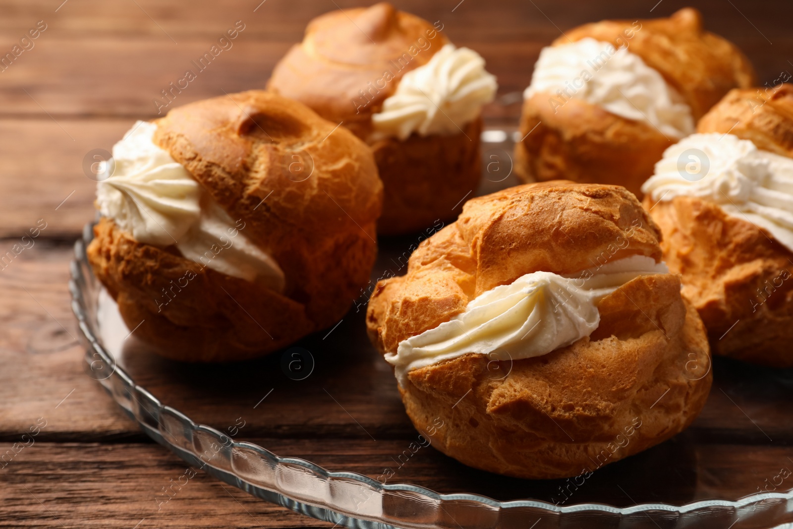 Photo of Delicious profiteroles with cream filling on wooden table, closeup