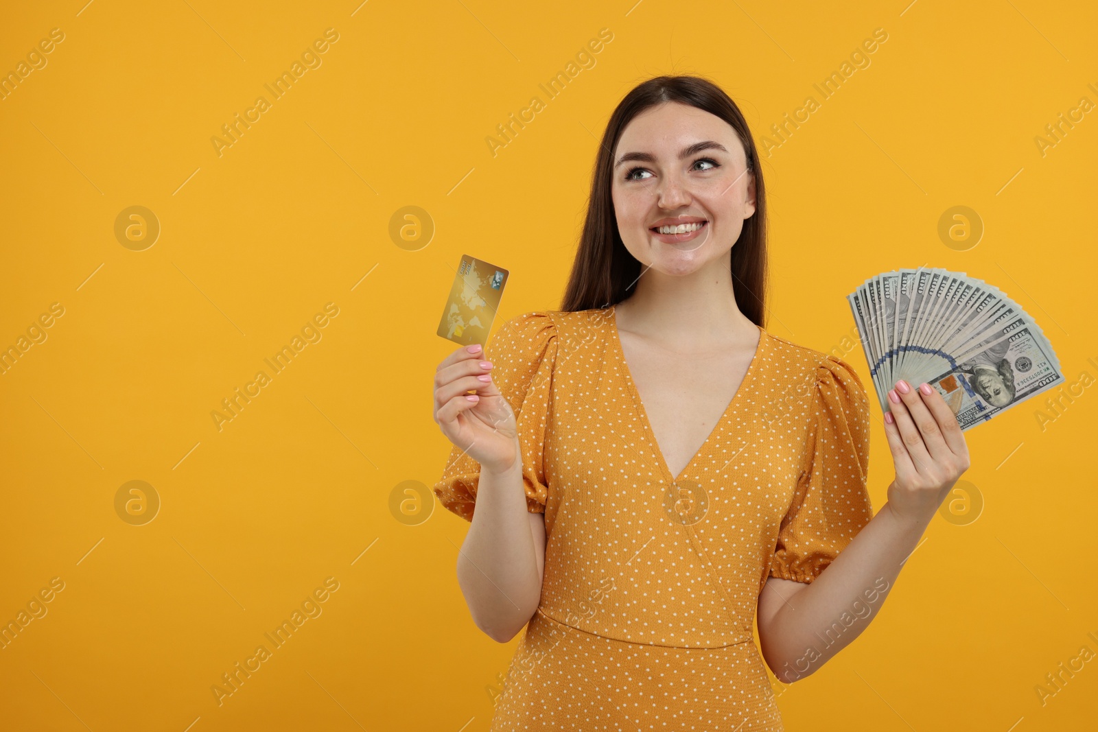 Photo of Happy woman with credit card and dollar banknotes on orange background, space for text