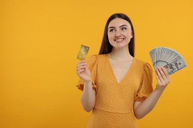 Happy woman with credit card and dollar banknotes on orange background, space for text