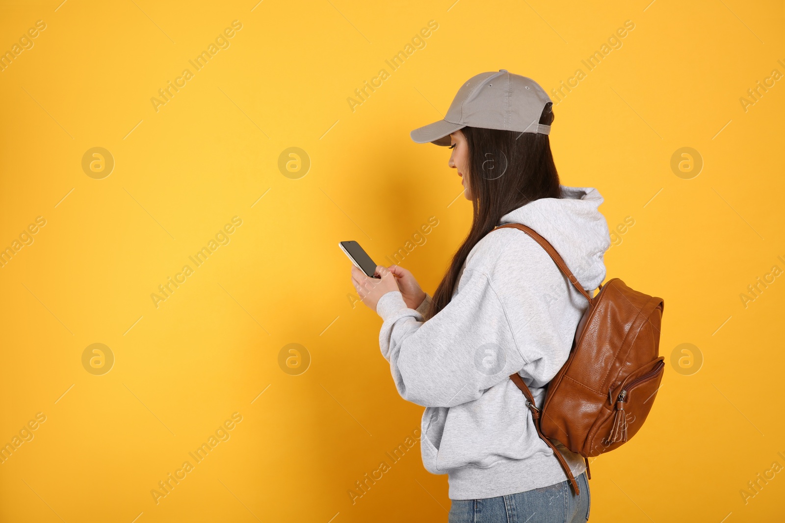 Photo of Beautiful young woman with stylish leather backpack and smartphone on yellow background. Space for text