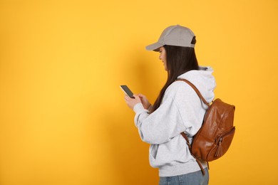 Photo of Beautiful young woman with stylish leather backpack and smartphone on yellow background. Space for text