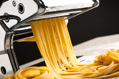 Photo of Pasta maker machine with dough on table against black background, closeup
