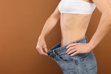 Slim woman wearing big jeans on brown background, closeup and space for text. Weight loss