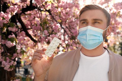 Photo of Man with pills and protective mask near blossoming tree outdoors. Seasonal pollen allergy
