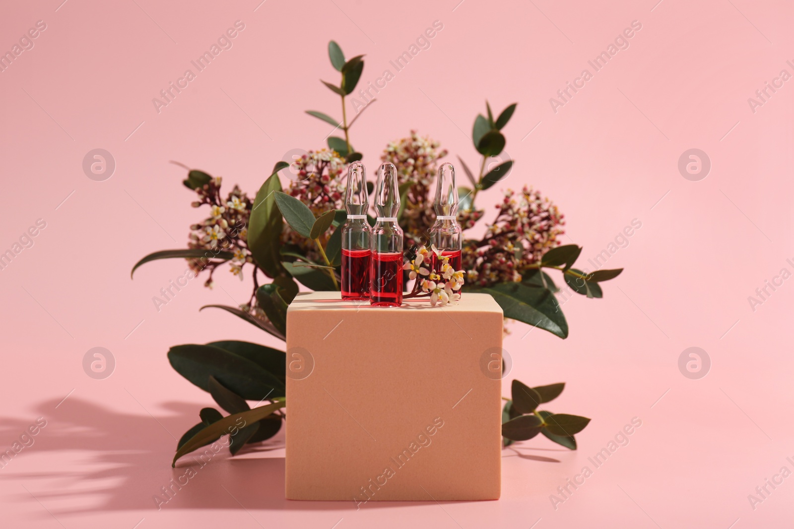 Photo of Stylish presentation of skincare ampoules and flowers on pink background