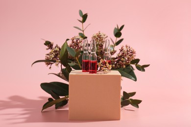 Photo of Stylish presentation of skincare ampoules and flowers on pink background