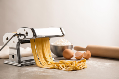 Photo of Pasta maker machine with dough on grey table. Space for text