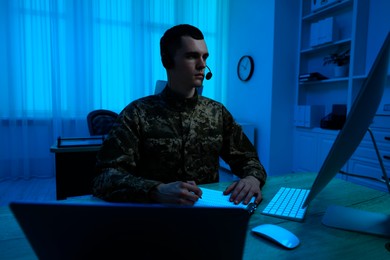 Military service. Soldier in headphones working at wooden table in office at night