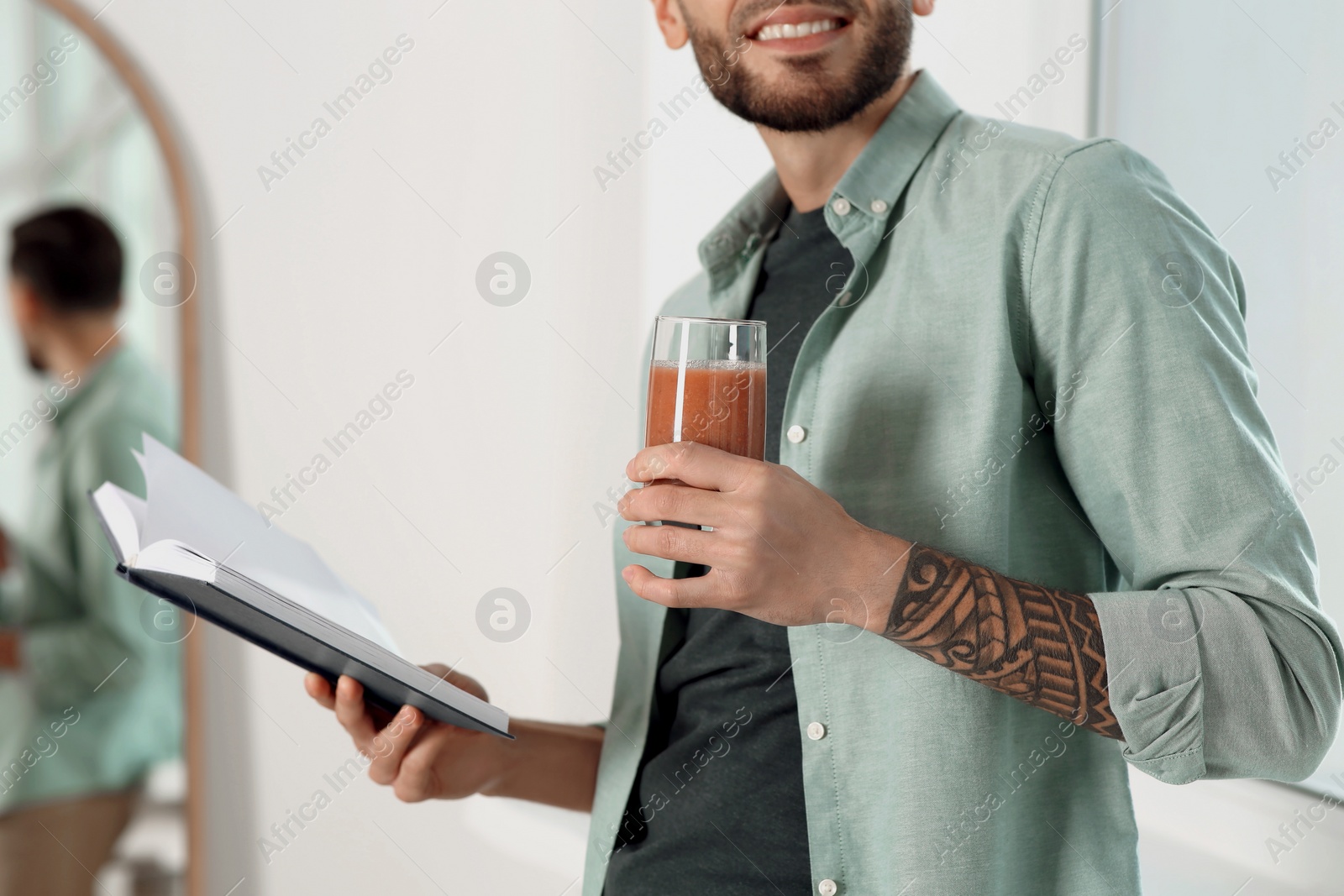 Photo of Man with delicious smoothie and book indoors, closeup