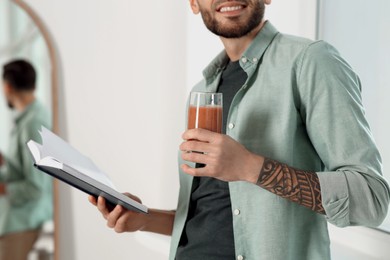 Photo of Man with delicious smoothie and book indoors, closeup