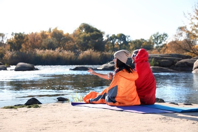 Photo of Campers sitting in sleeping bags on wild beach. Space for text