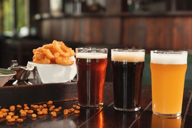 Photo of Glasses of tasty beer and snacks on wooden table in bar