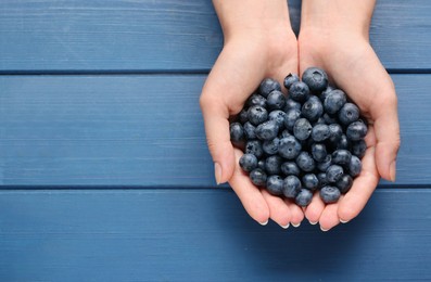 Photo of Woman with heap of tasty blueberries on blue wooden background, top view. Space for text