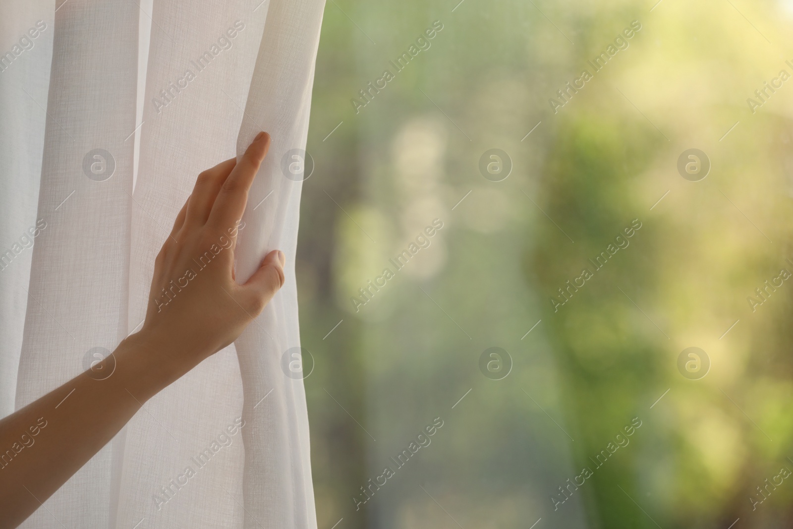 Photo of Woman opening white window curtains in room, closeup. Space for text