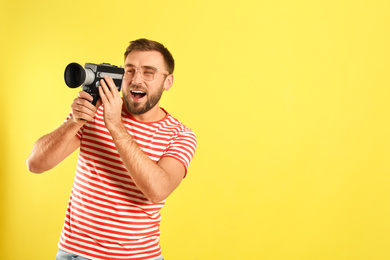 Young man with vintage video camera on yellow background, space for text