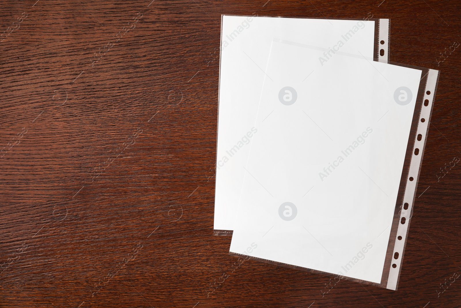 Photo of Punched pockets with paper sheets on wooden table, flat lay. Space for text